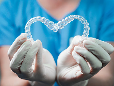 A dental hygienist s hand holding a transparent heart-shaped object, possibly a dental appliance or model, while wearing gloves.