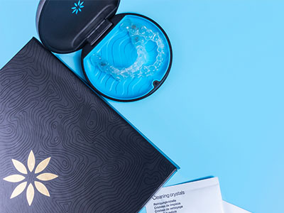 The image shows a blue toothbrush with a box of dental floss next to it on a light blue surface, with a closed book featuring an abstract design in the background.