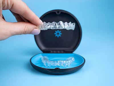 An individual s hand holding an open, blue-colored plastic case containing multiple clear braces with teeth-like structures.